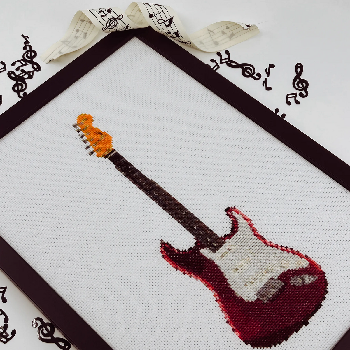 Cross-stitch of a red fender strat guitar on white fabric