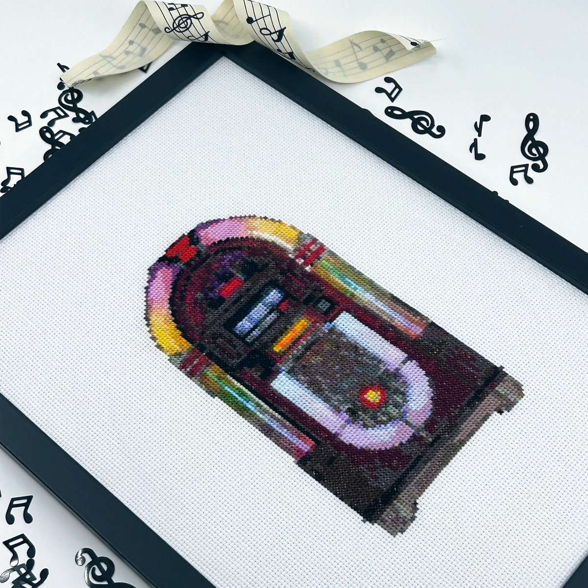 Cross-stitched artwork of a vintage jukebox on white fabric framed