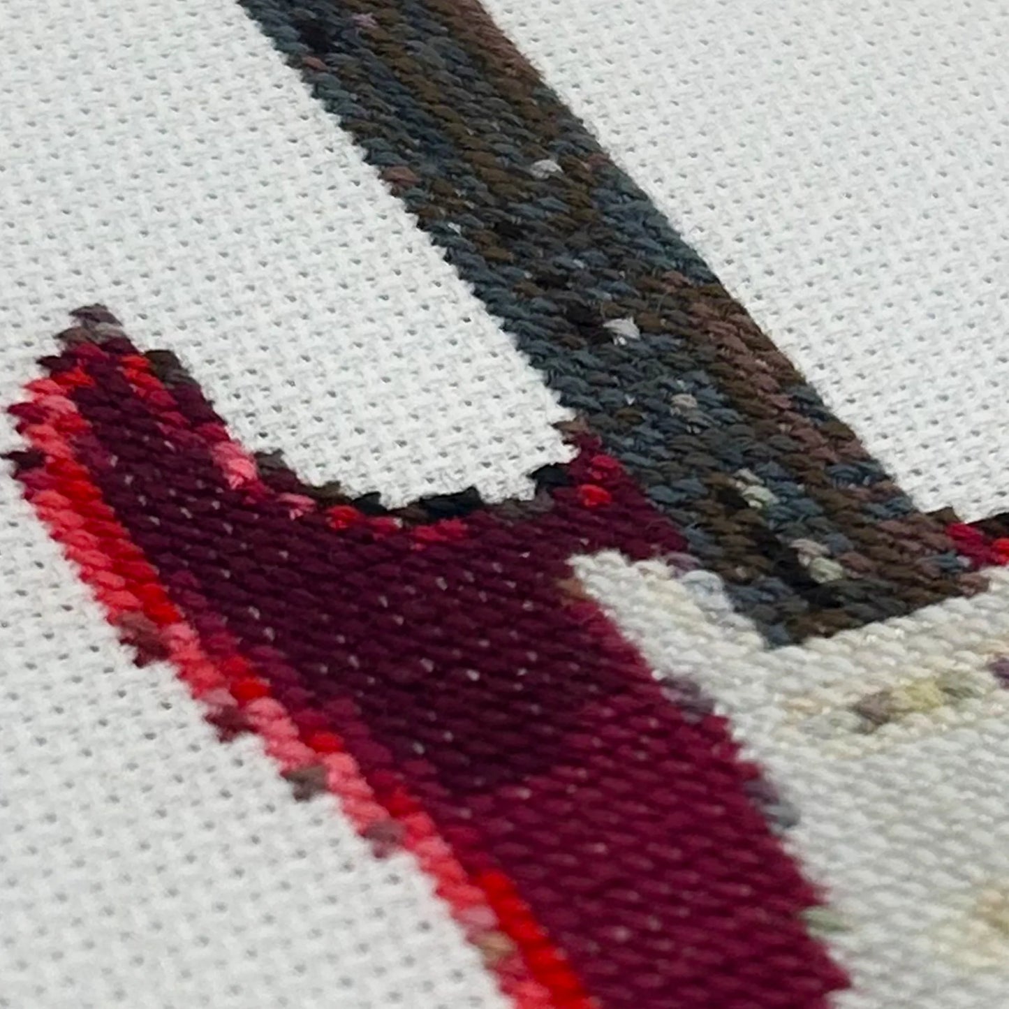 Close up of cross stitch of a fender stratocaster guitar on white fabric