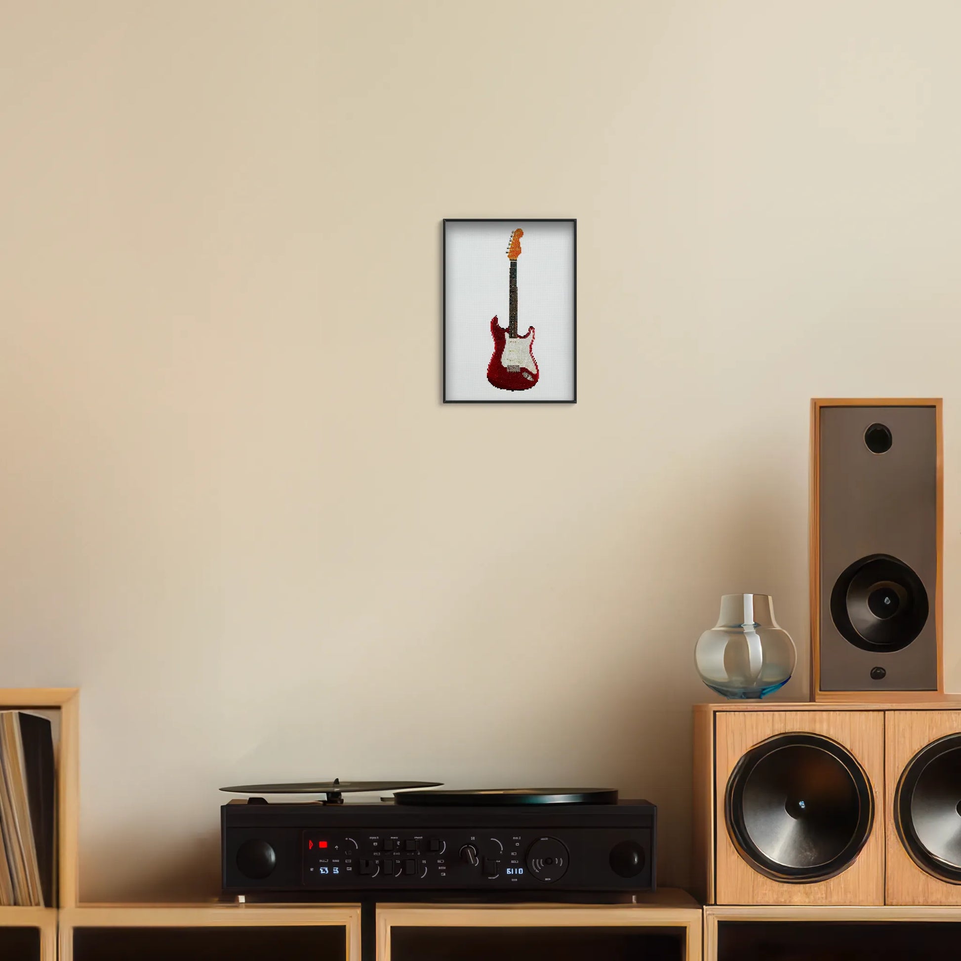 A5 print of the original embroidery design of a fender strat framed and hung up on a wall above a record player