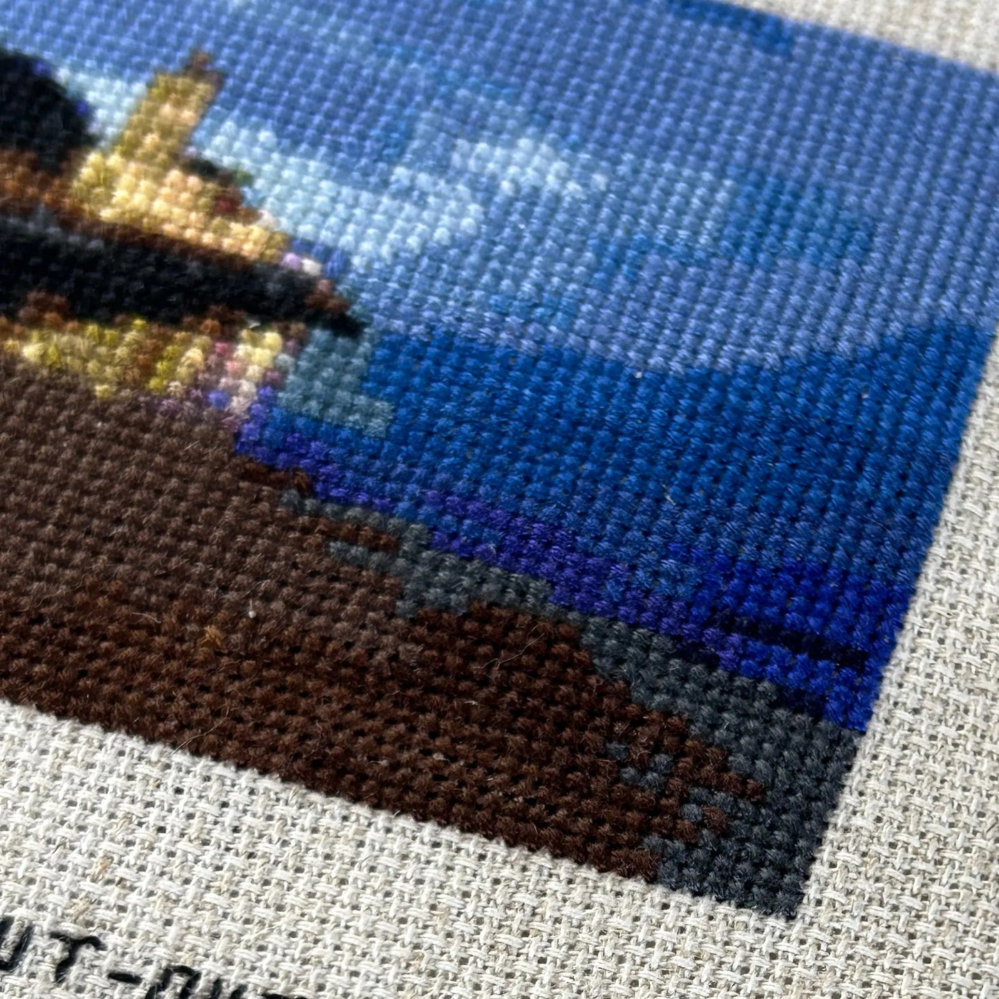 Close up of the sky, beach and church cross stitch in the evening in Gijon, Asturias, Spain. On rustic Aida fabric.