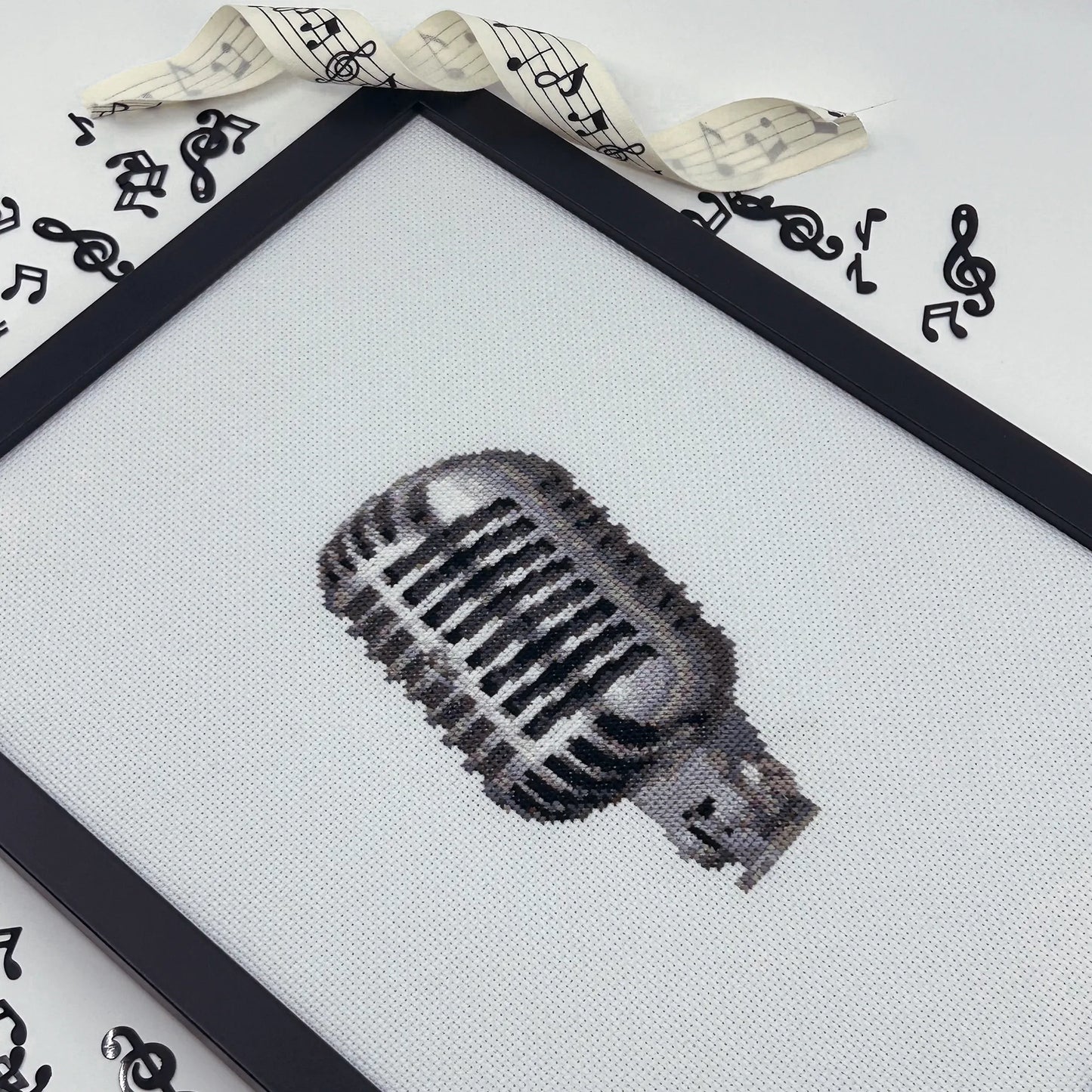 Cross-stitched retro microphone design on white fabric in a black frame.