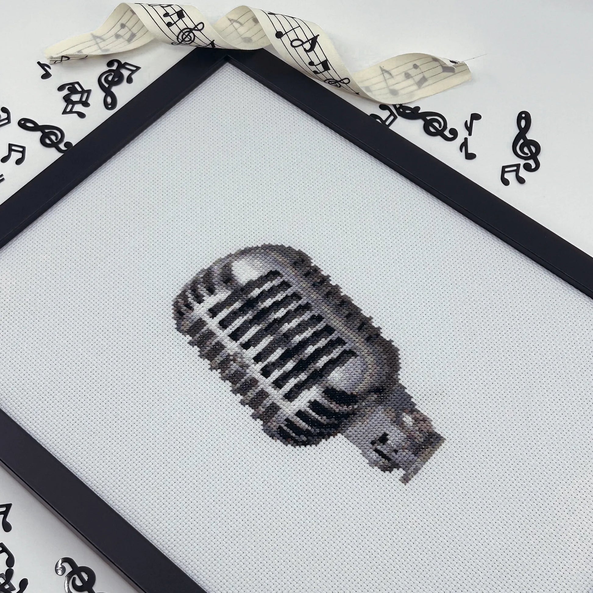 Cross-stitched retro microphone design on white fabric in a black frame.