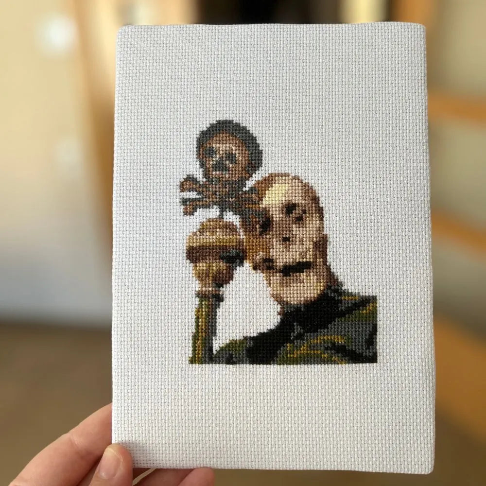 Unframed robed skeleton embroidery mounted and held up in hand.