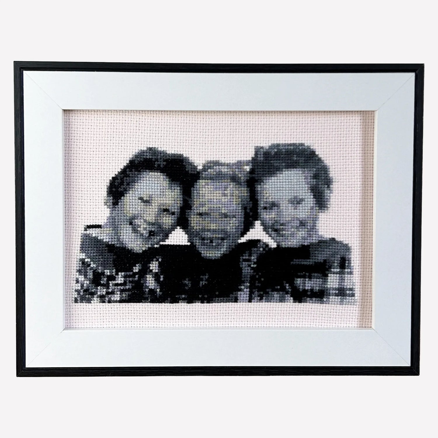Framed black and white cross stitch custom embroidery of three young sisters on a plain background